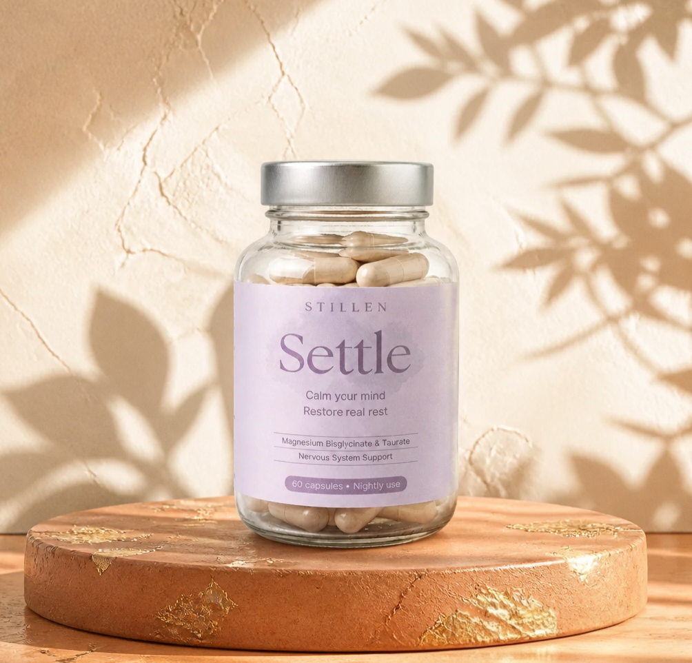 Glass jar of 'Settle' supplements with a purple label on a wooden surface.
Stillenhealth