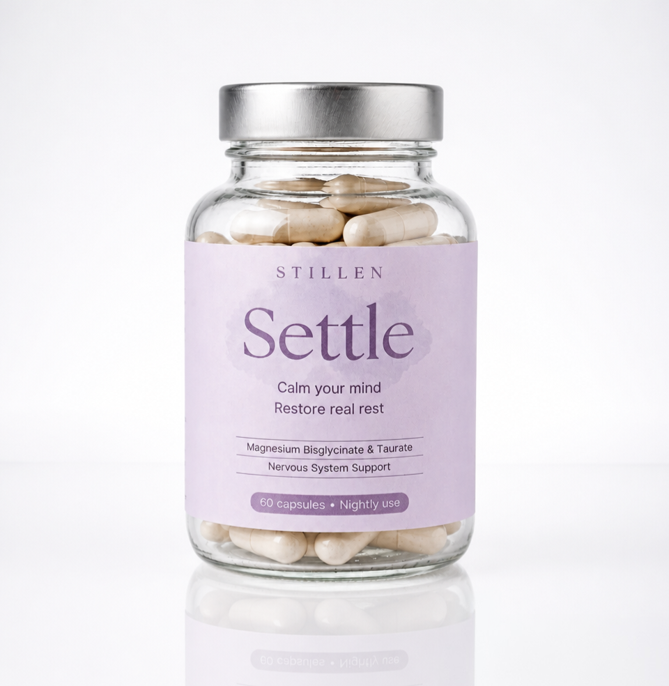 A clear glass supplement bottle with a silver metal lid and a lavender label reading 'STILLEN Settle' on a clean white background.