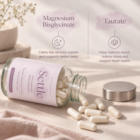 A clear glass bottle of Stelle Magnesium Bisglycinate capsules lies on its side with several capsules spilled out, alongside the silver cap. The scene is styled with a soft beige fabric and a small plant in the background, with text overlays describing the benefits of Magnesium Bisglycinate and Taurate.