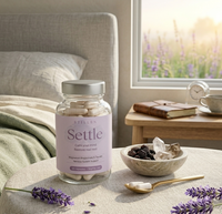 Bottle of 'Settle' magnesium supplements on a table with lavender flowers and a window in the background.
Stillenhealth